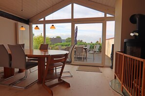 Ein Essbereich mit Tisch und Stühlen, einer Holzbalkendecke und Blick durch große Fenster auf eine Terrasse.