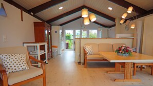 Amplia habitación con una mesa de comedor de madera, dos sillas, un sofá y una zona de cocina con ventana.