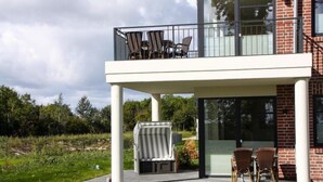 A modern two-story building with a balcony, outdoor seating, and a grill area. - Appartements im Avalon Hotel Bellevue, Fehmarn (Fehmarn)
