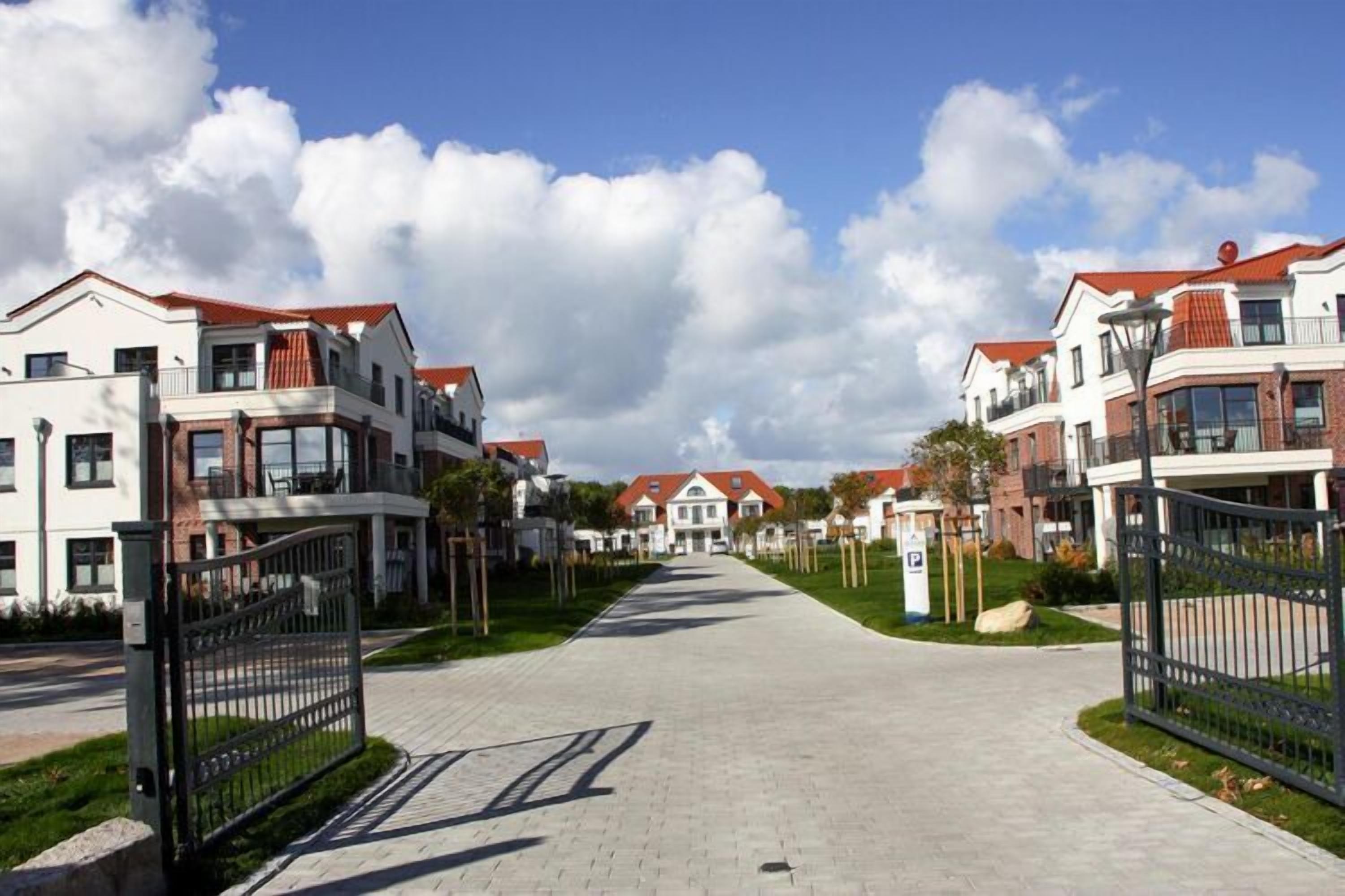 A residential street with modern houses, a paved walkway, and a gated entrance.