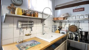 A kitchen with a wooden countertop, a white sink, hanging utensils, and a clock on the wall.