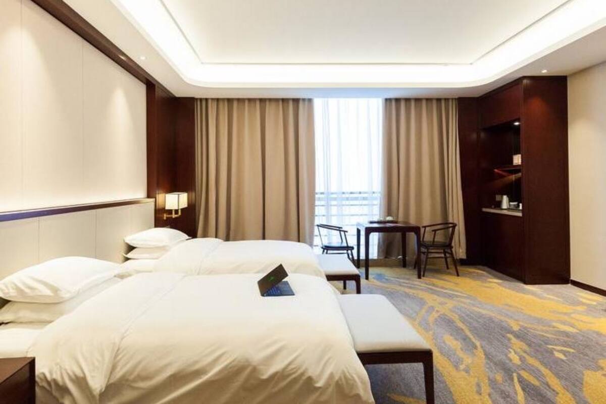 Ein Hotelzimmer mit einem großen Bett, einem Schreibtisch, zwei Stühlen und Blick auf die Stadt durch das Fenster.