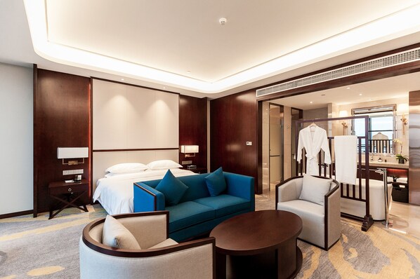 Una habitación de hotel moderna con una cama, un sofá azul, una mesa de centro redonda y una zona de estar con una silla.