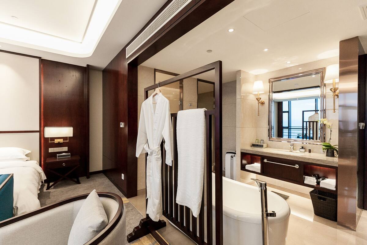 Ein modernes Hotelbad mit Badewanne, großem Spiegel und Bademäntelständer.