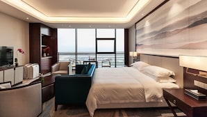 A modern hotel room with a large bed, a desk, a chair, and a view of the sea through large windows. - Jinyi Jinglan Hotel (Jinhua)