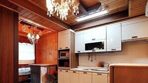 A kitchen with wooden walls, a chandelier, white cabinets, and a microwave. - Beach Terrace Pension Taean (Taean)