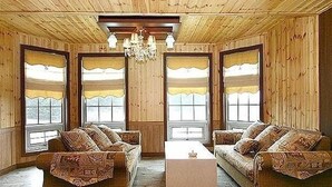 A room with wooden walls and ceiling, two sofas with patterned cushions, a chandelier, and large windows with curtains. - Beach Terrace Pension Taean (Taean)