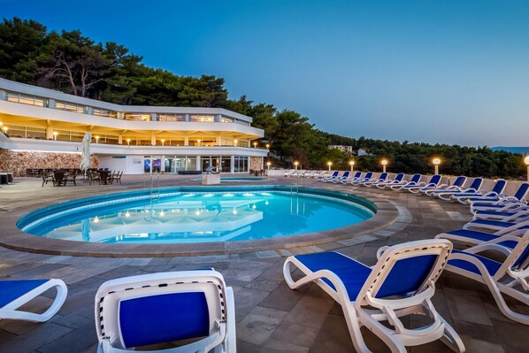 Un espace piscine avec des chaises longues et un bâtiment à plusieurs étages doté de balcons.