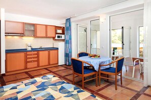 Cocina compacta con armarios de madera, microondas y cafetera. Cuenta con una zona de comedor con mesa y sillas, además de un tapete estampado.