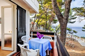 Un balcon avec une table et des chaises, donnant sur une zone côtière bordée d’arbres et offrant une vue sur la mer.