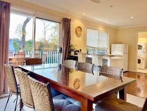 A dining area with a glass table and wicker chairs, a kitchen with a sink and appliances, and a view through large windows.