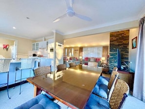 A modern living room with a dining table, sofas, and a kitchen area.
