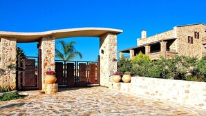 A stone building with a large entrance gate, potted plants, and a clear blue sky. - Cretan Villa Near Beach for 10 (Kondomari)