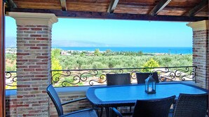 A covered patio with a table and chairs, a lantern, and a view of the sea and landscape. - Cretan Villa Near Beach for 10 (Kondomari)