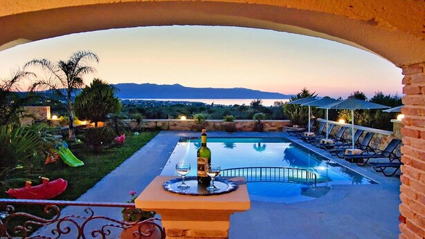 A pool area with a view of mountains, lounge chairs, and a table with a bottle and glass. - Cretan Villa Near Beach for 10 (Kondomari)