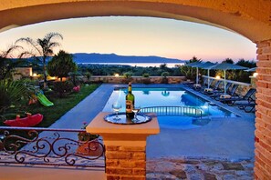 A pool area with a view of mountains, lounge chairs, and a table with a bottle and glass.