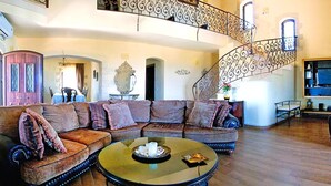 A spacious living area with a large sectional sofa, a round coffee table, and a staircase with ornate metal railings. - Cretan Villa Near Beach for 10 (Kondomari)