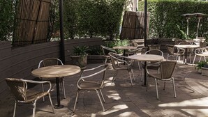 Ein Patio im Freien mit runden Tischen und Korbstühlen, umgeben von Pflanzen und Bambusarchitektur.