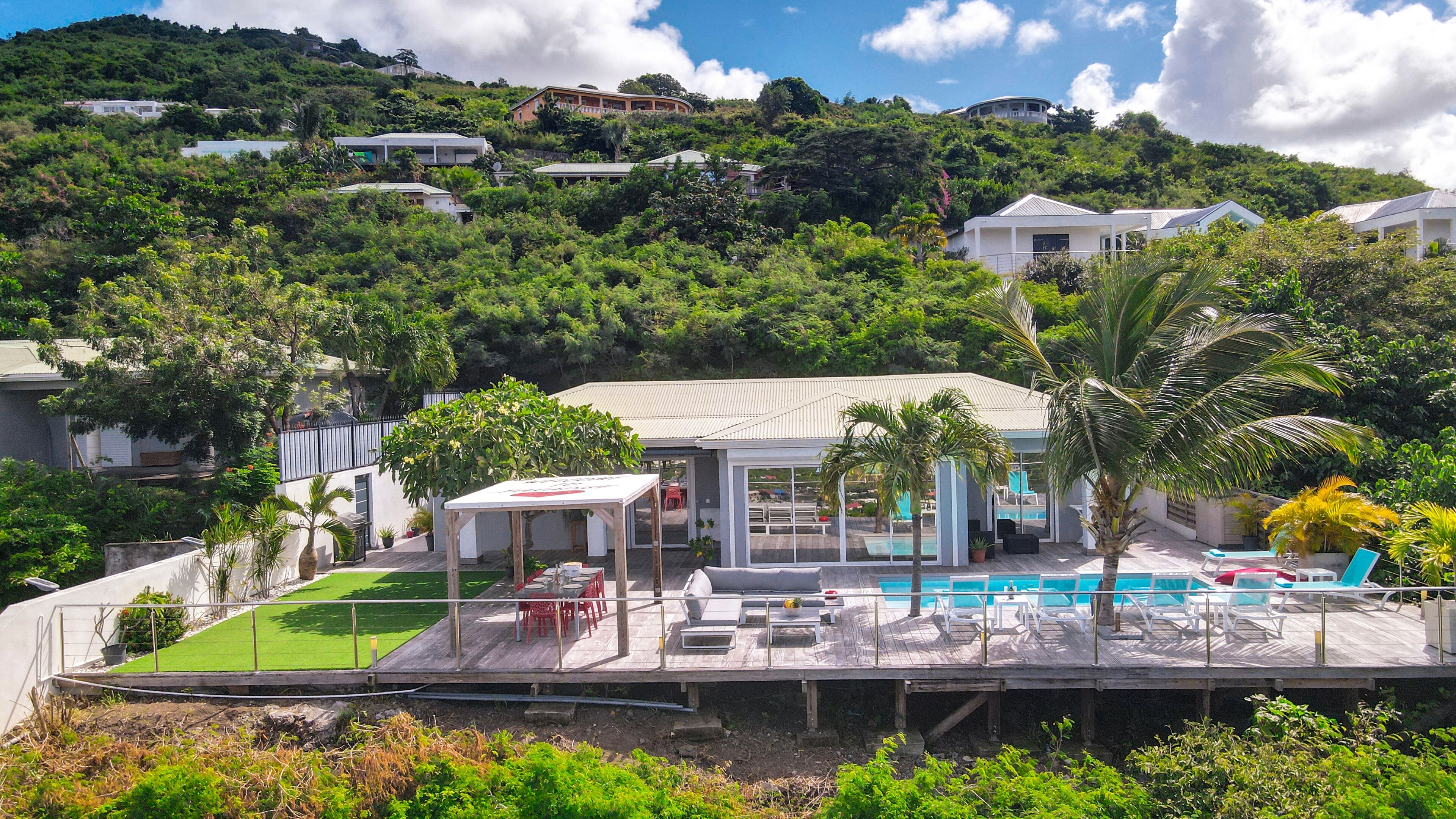 A modern house with a pool, surrounded by lush greenery and hills.