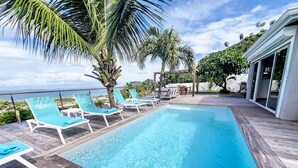 A swimming pool with lounge chairs and palm trees, surrounded by a wooden deck and a view of the ocean. - Villa SEA VIEW, 5' from Grand Case Beach, private pool, huge privacy (saint martin)