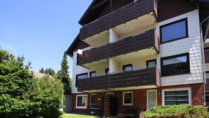 Un edificio residencial de varios pisos con un balcón en el segundo nivel, fachada de ladrillo y cielo despejado.