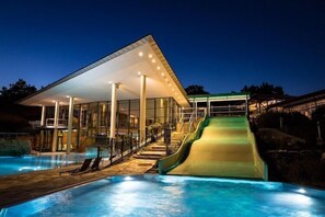 A modern building with a glass facade, a pool, and a green slide.