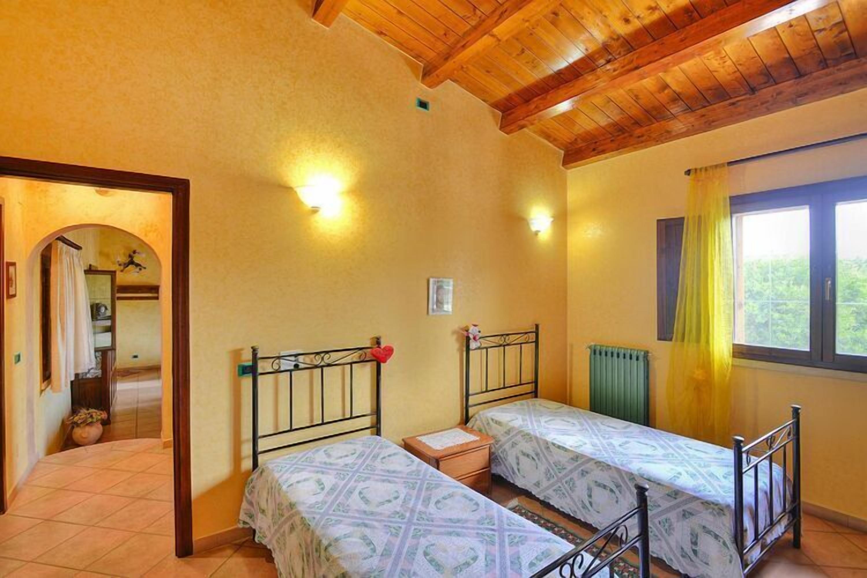 Une chambre avec deux lits, des poutres apparentes en bois au plafond et une fenêtre ornée de rideaux jaunes.