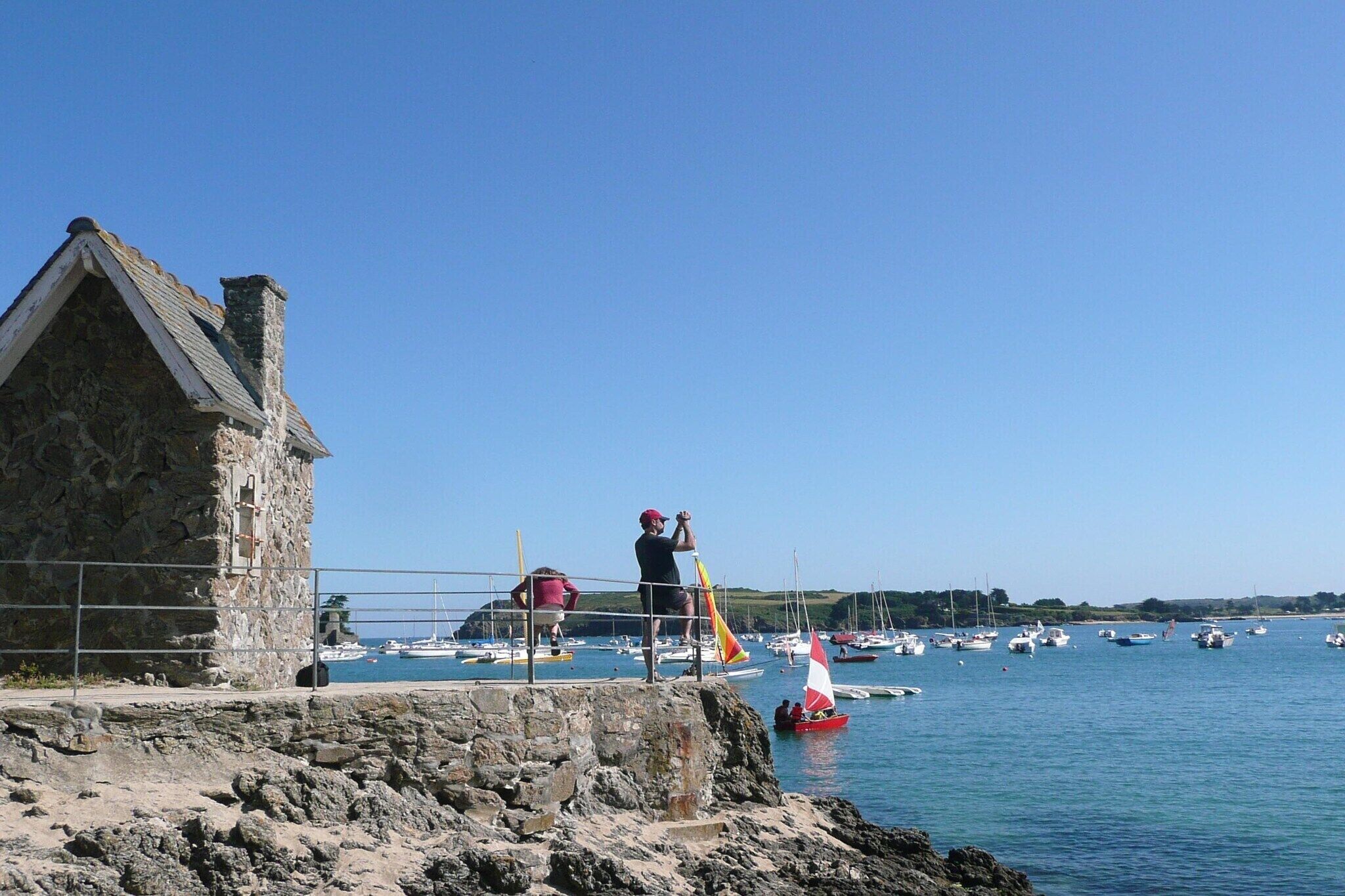 A stone building with a sloped roof near a body of water with several boats.