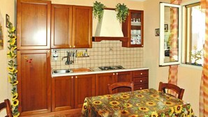 A kitchen with wooden cabinets, a tiled backsplash, a sink, and a dining table with a sunflower tablecloth. - Holiday Home Floridia with Pool near Beach (Siracusa)
