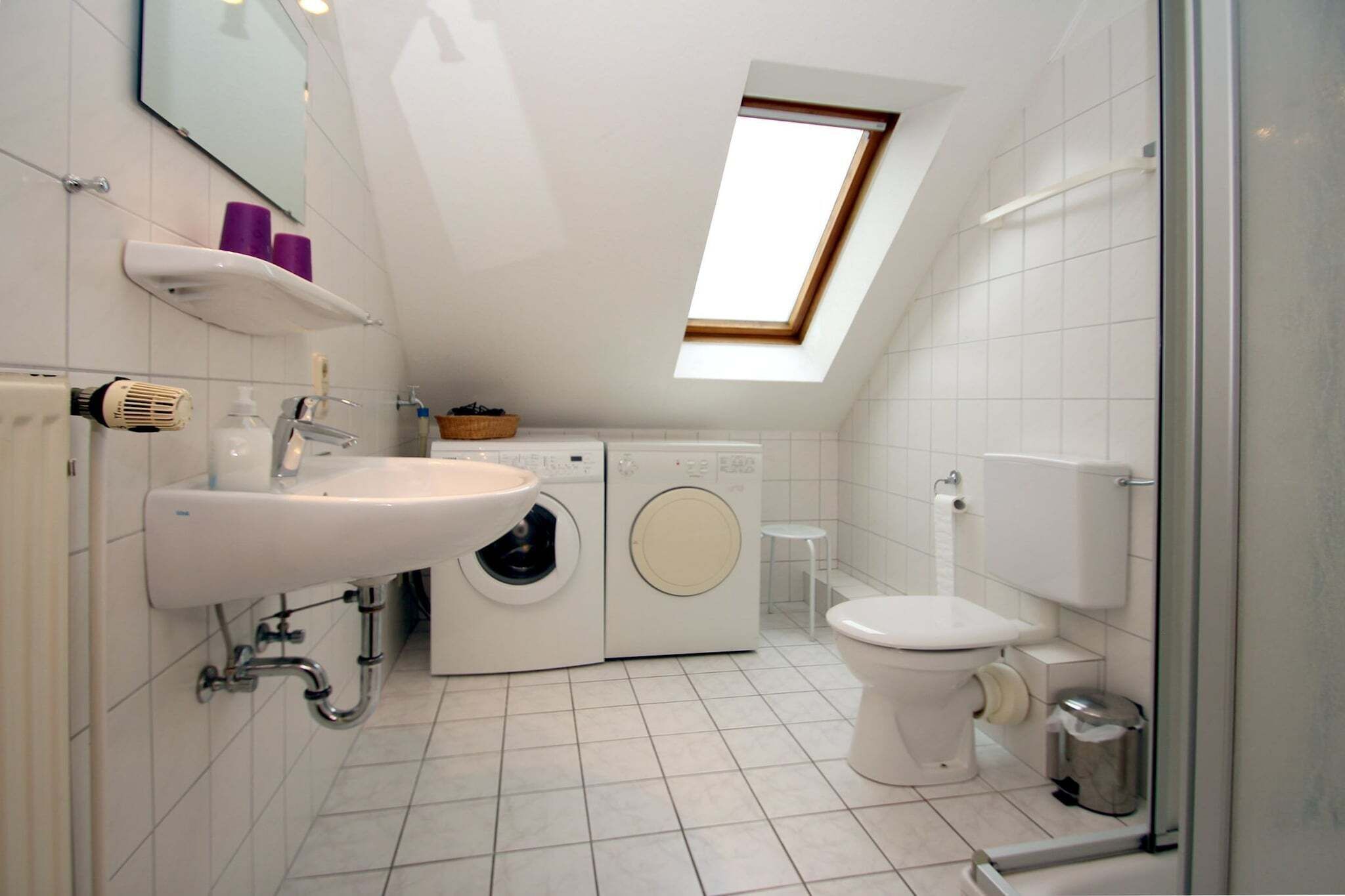 Un baño moderno y compacto con tragaluz, lavadora, inodoro y lavamanos.