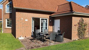 Ein Backsteinhaus mit Ziegeldach, einer Terrasse mit Tisch und Stühlen sowie einem kleinen Garten.