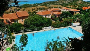 Piscina rodeada por casas com telhados vermelhos, com uma montanha e o mar ao fundo.
