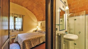 A bedroom with a bed, a nightstand, a lamp, and a bathroom with a sink and shower. - Country House in Tuscany with Pool and Tennis (Santo Pietro Belvedere)