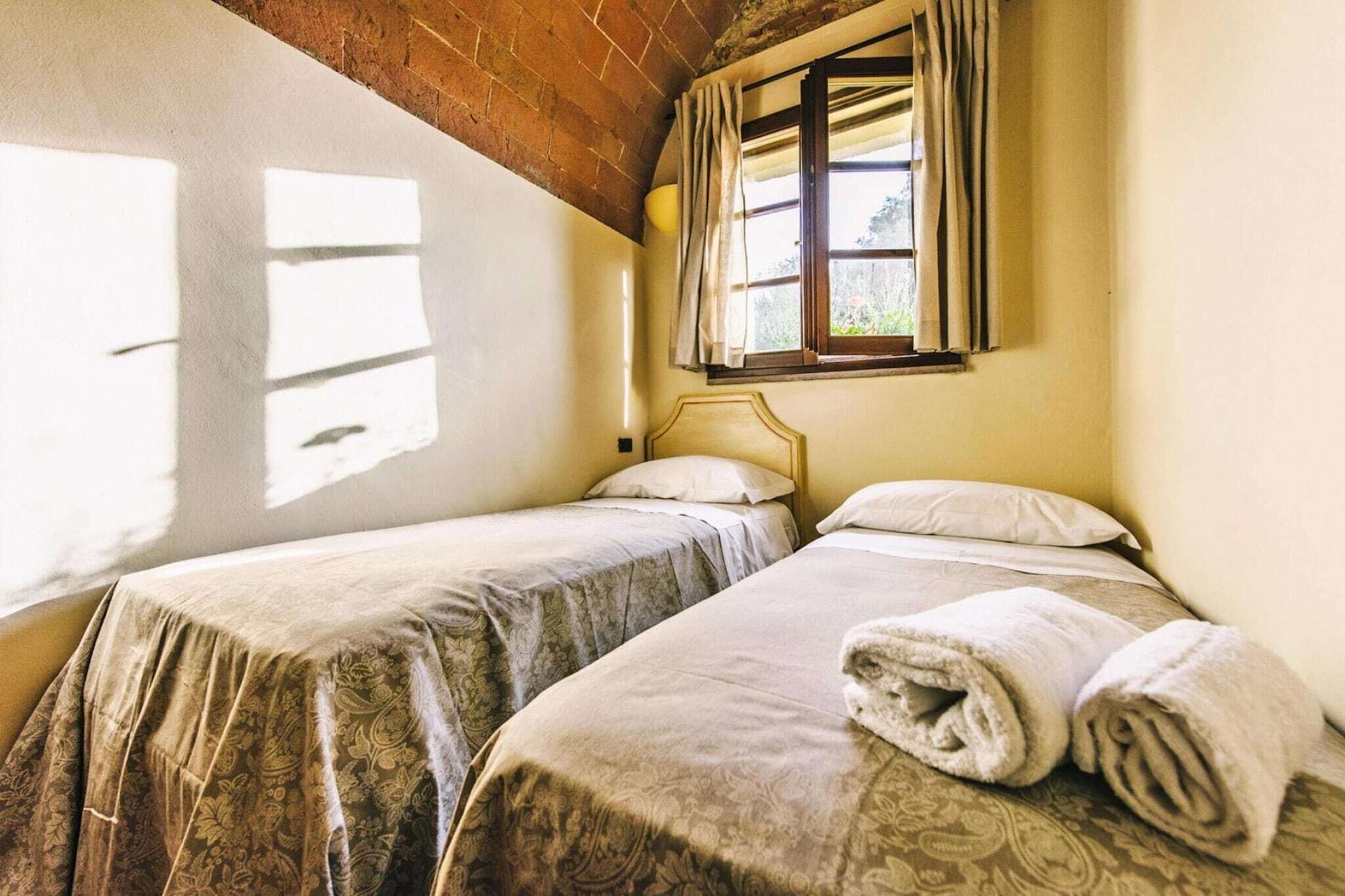 Una habitación con dos camas, una ventana con cortinas y una toalla sobre la cama.