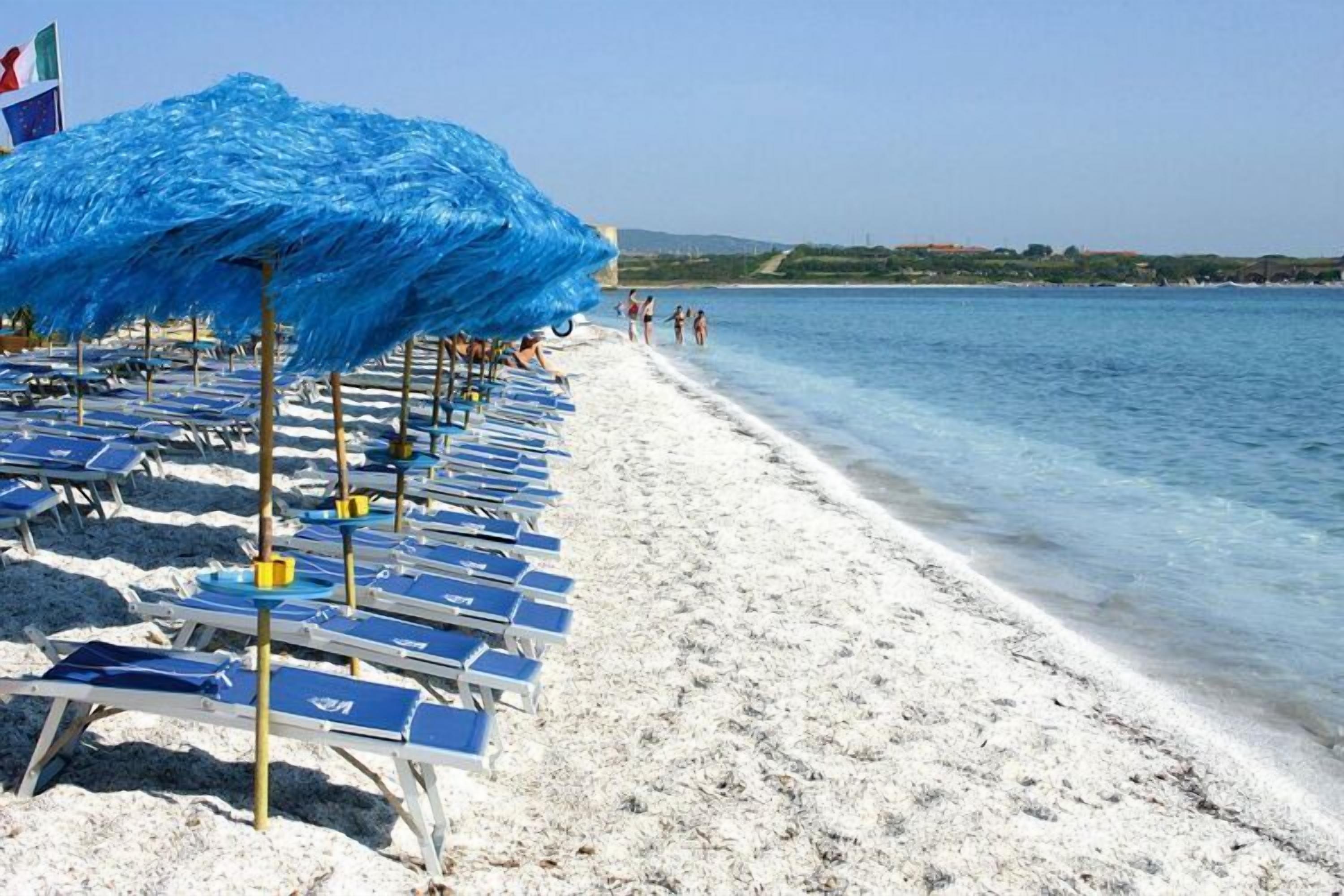 Een strand met rijen ligbedden en parasols, een heldere blauwe zee en een verre kustlijn.