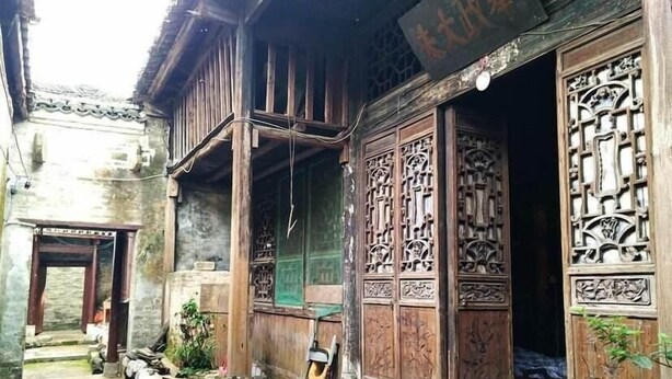 A traditional wooden building with intricate carvings on the doors and walls, a small outdoor seating area, and a visible staircase leading to the entrance. - Natural Lodge Homestay (Guilin)