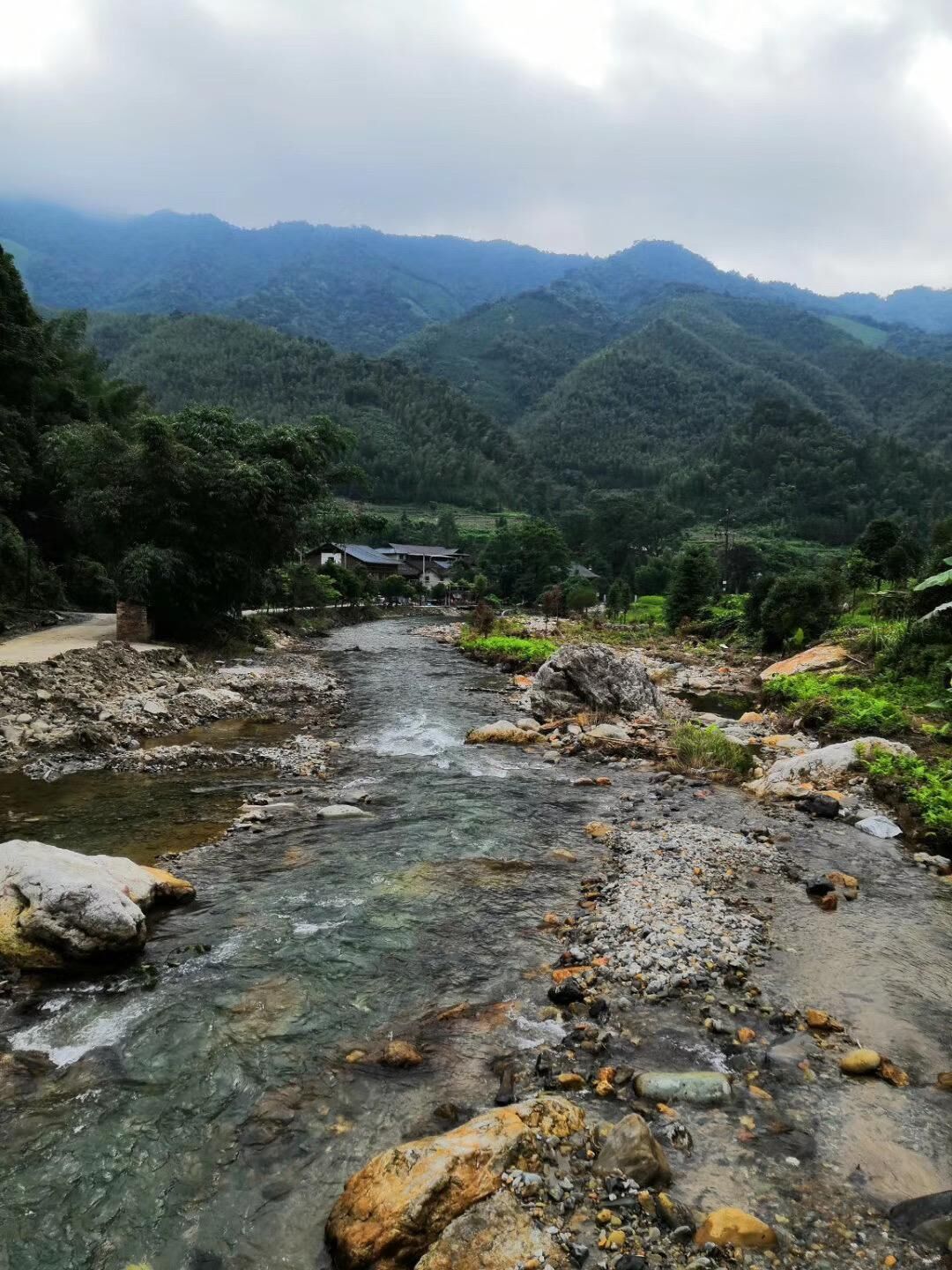 A river flowing through a mountainous area with a small building in the distance.