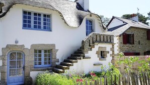 Une maison traditionnelle en pierre, avec une façade blanche, des fenêtres à cadre bleu et un escalier en pierre menant à l’entrée.