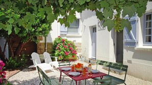 Une table dressée pour quatre personnes, avec une nappe rouge, des chaises blanches et un panier de fruits.