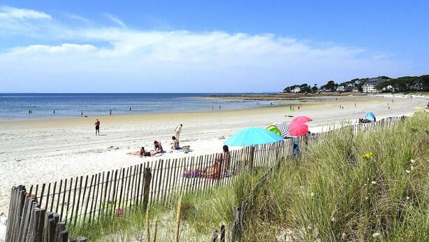 Une plage avec une clôture en bois, des parasols et des gens qui prennent un bain de soleil.