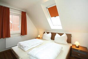 A bedroom with two beds, a skylight, a window with curtains, bedside lamps, and a radiator.