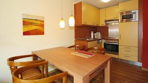 A compact kitchen with wooden cabinets, a dining table with chairs, and a painting on the wall.