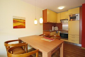 A compact kitchen with wooden cabinets, a dining table with chairs, and a painting on the wall.