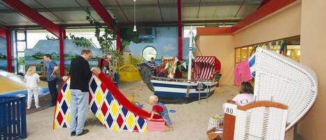 An indoor play area with a slide, a boat play structure, and a wicker chair.