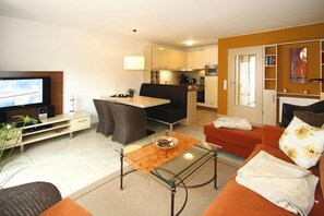 A compact living space with a television, seating area, kitchenette, and a dining table.