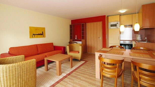 A compact living space with a sofa, a dining table with chairs, a kitchen area with a microwave, and a red accent wall.