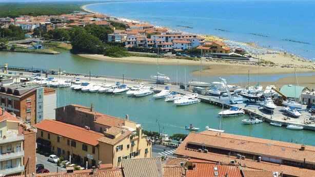 Un puerto deportivo con barcos amarrados, una playa y edificios con techos de tejas rojas.