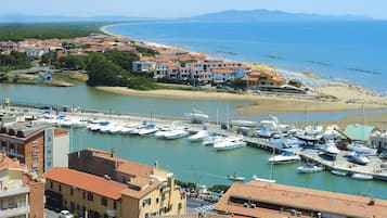 A marina with boats docked, a beach, and buildings with red-tiled roofs.