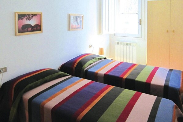 A room with two beds, each with a striped blanket, a window with blinds, and a radiator.