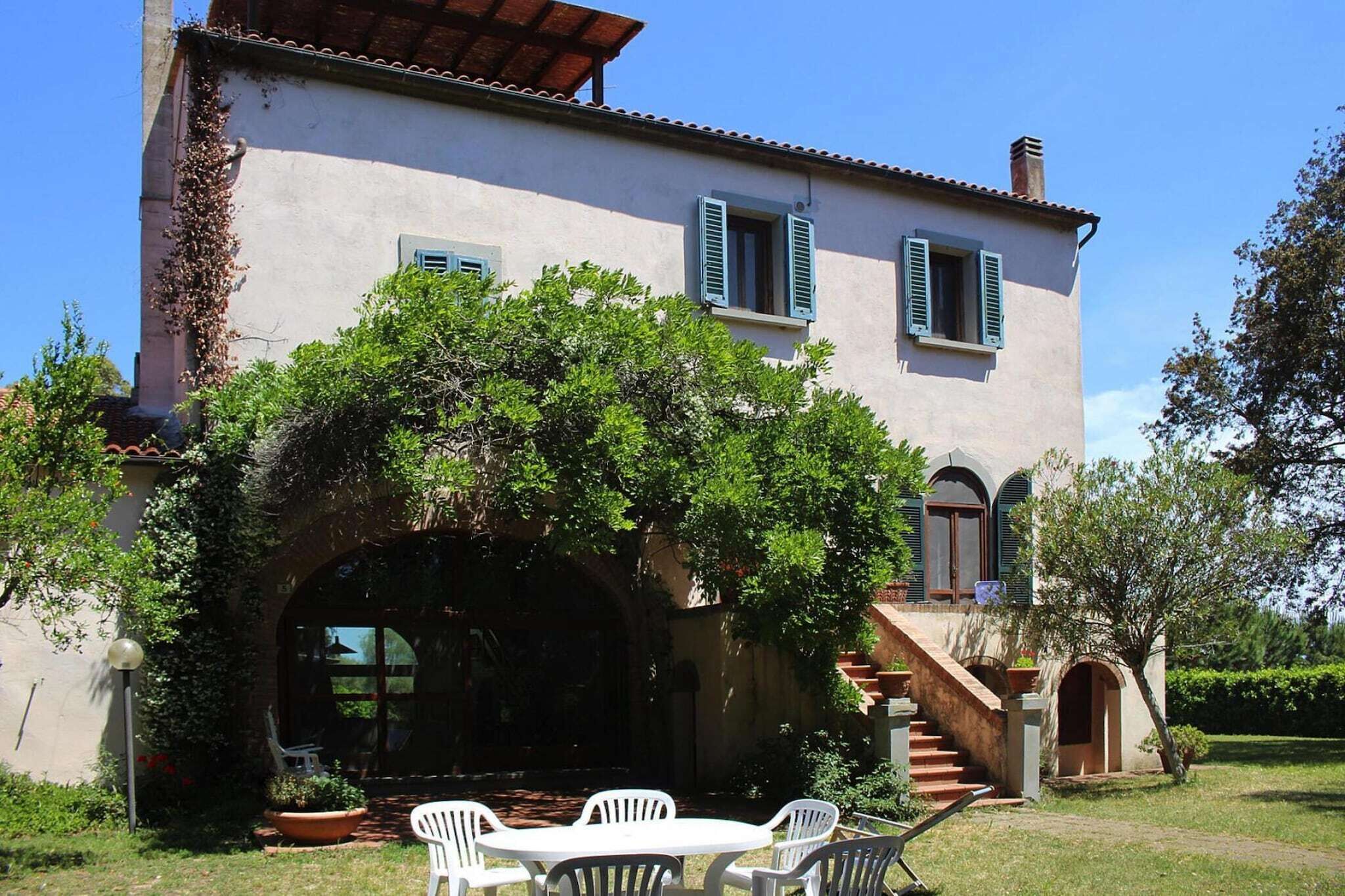A two-story house with a covered patio, a staircase leading to the upper floor, and a garden area with a table and chairs.